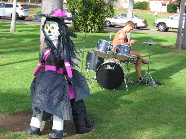 Not sure why a drummer is sitting alone on the grass. Perhaps the witch is a singer, and the band is resting during intermission.