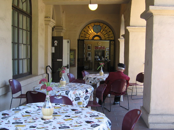 A lone gentlemen sits at a cafe table outside the House of Italy in Balboa Park.